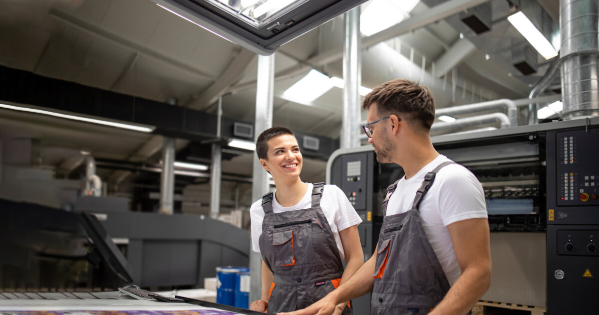 Male and female coworkers smiling in overalls at a factory.